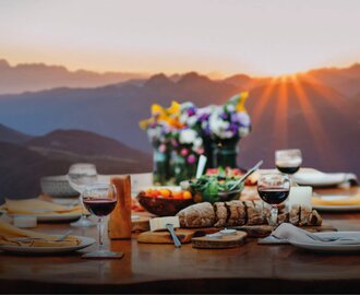 Wooden table with wine, bread, cheese and flowers at mountain dinner during sunset