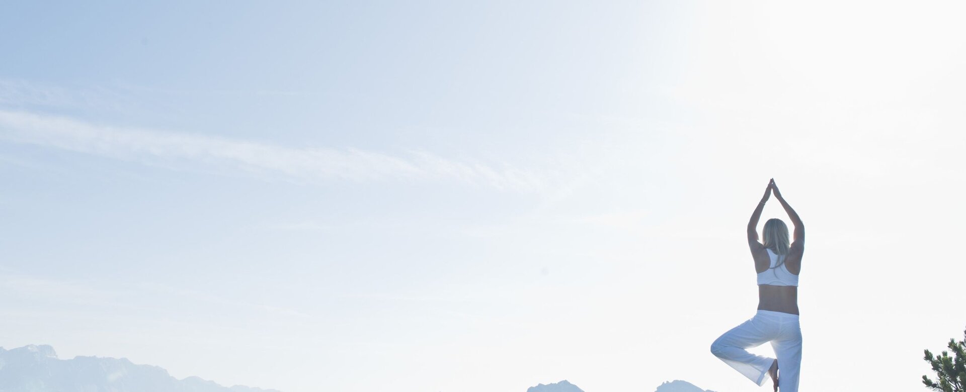 Person in white clothes doing yoga on rock with view of sunny mountain landscape