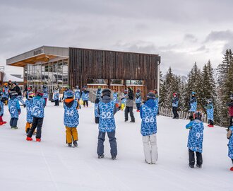 Many kids in blue vests standing in snow near lodge during ski camp session. | © Shuttleberg / Absolut Park