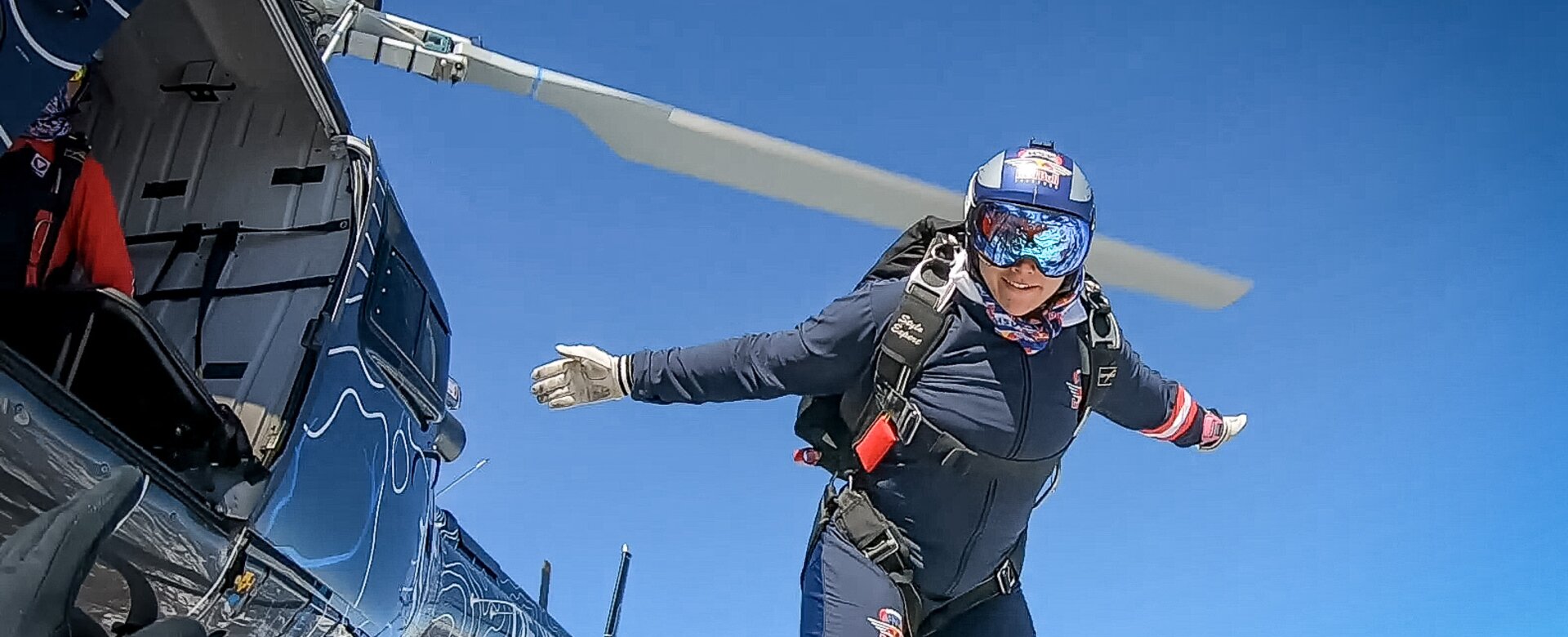 Eine Dame mit einem Fallschirmrucksack springt gerade aus einem Helikopter  | © Snow Space Salzburg