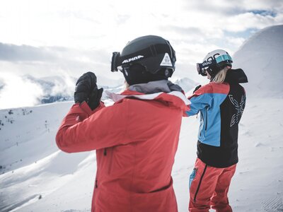 Two skiers in snow gear with helmets and goggles do yoga while overlooking the valley. | © Gasteinertal Tourismus GmbH, Klaus Listl - Freezing Motions WEB