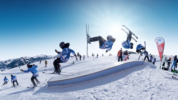 A freeskier does a frontflip over a rail at Cash4Tricks during RIDE Ski amadé, captured as a multiple-frame sequence.