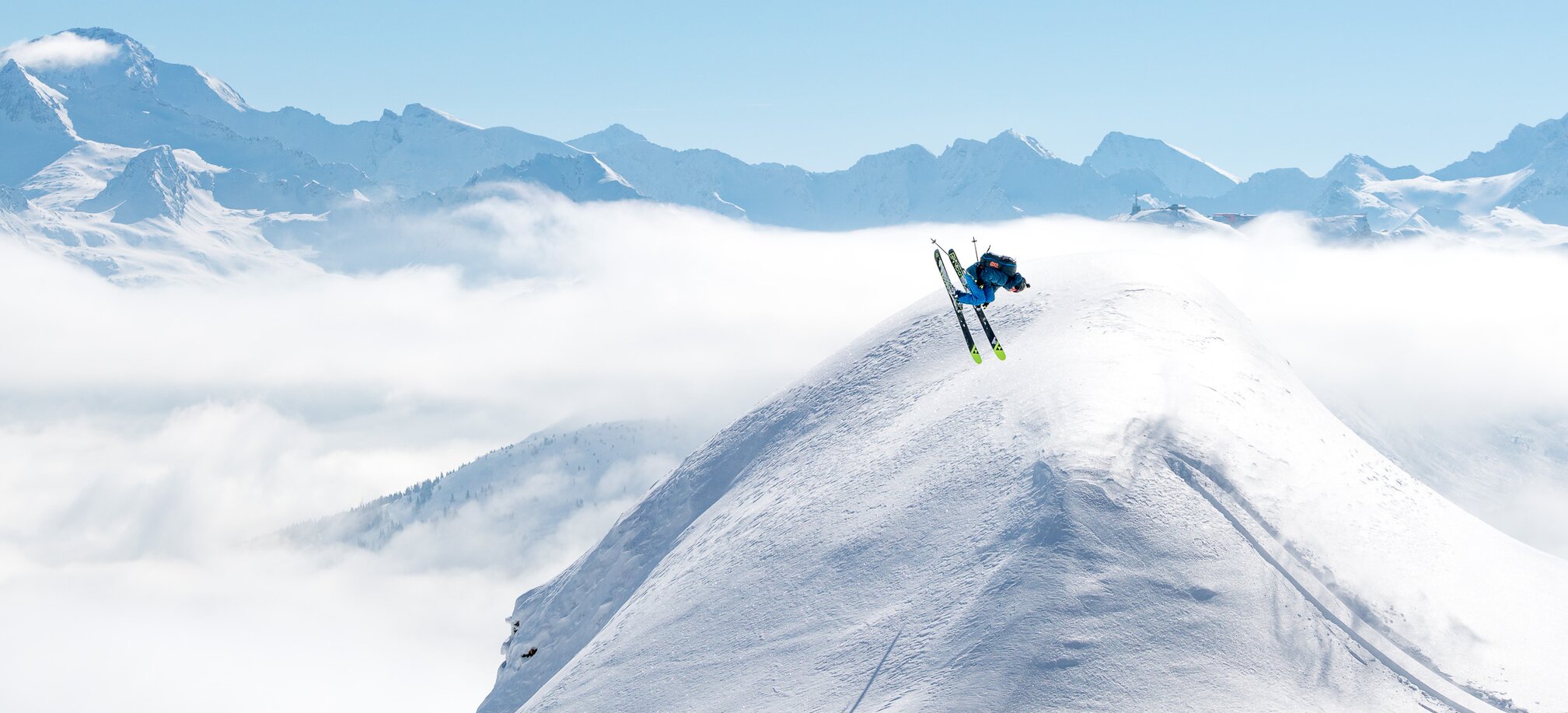 Skier doing a backflip over a snow dome and all around are snowy mountains and a blue sky | © Gasteinertal Tourismus GmbH, www.oberschneider