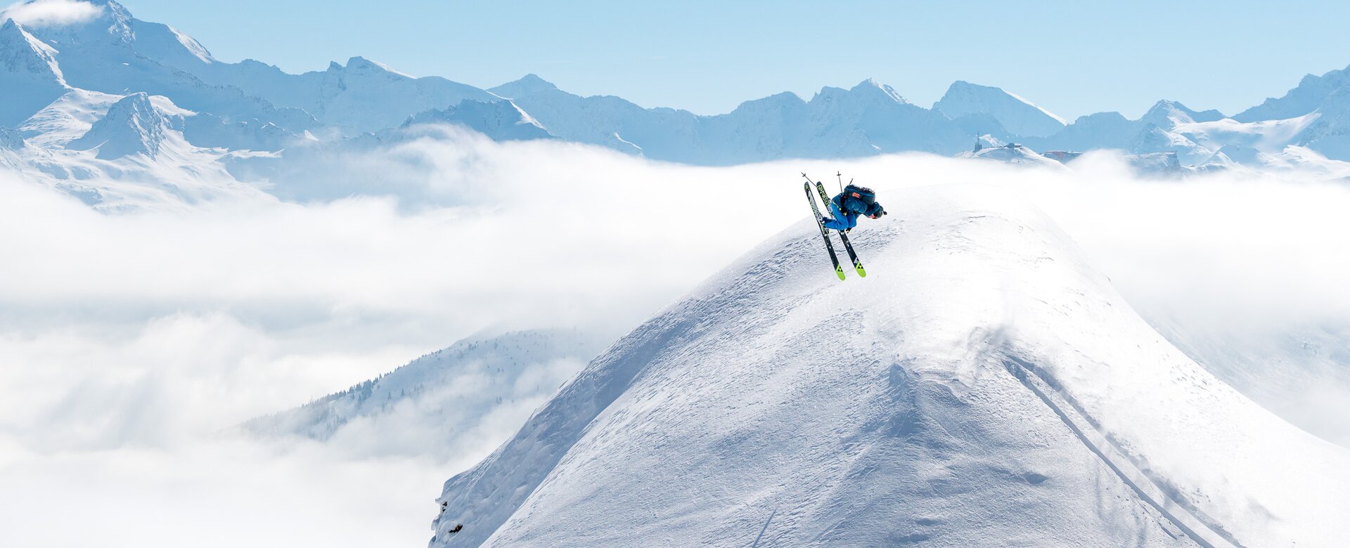 Skier doing a backflip over a snow dome and all around are snowy mountains and a blue sky | © Gasteinertal Tourismus GmbH, www.oberschneider