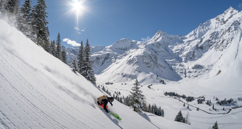 Skier freeriding in open terrain with sunlit snow-covered mountains in the background | © Gasteinertal Tourismus GmbH | Christoph Oberschneider