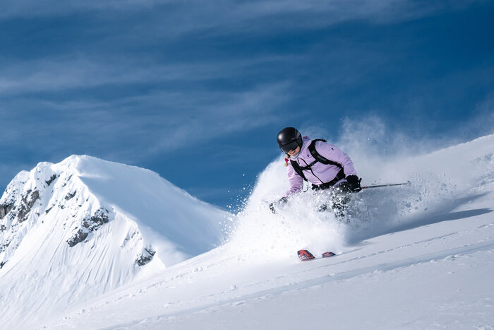 Female skier in helmet rides downhill in deep snow, powder spraying during dynamic carving turn | © Liftgesellschaft Zauchensee/C.Schartner