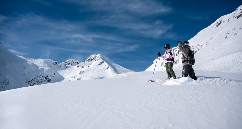 Two freeriders with helmets and backpacks stand in deep snow, facing snowy alpine mountain peaks | © Liftgesellschaft Zauchensee/C.Schartner