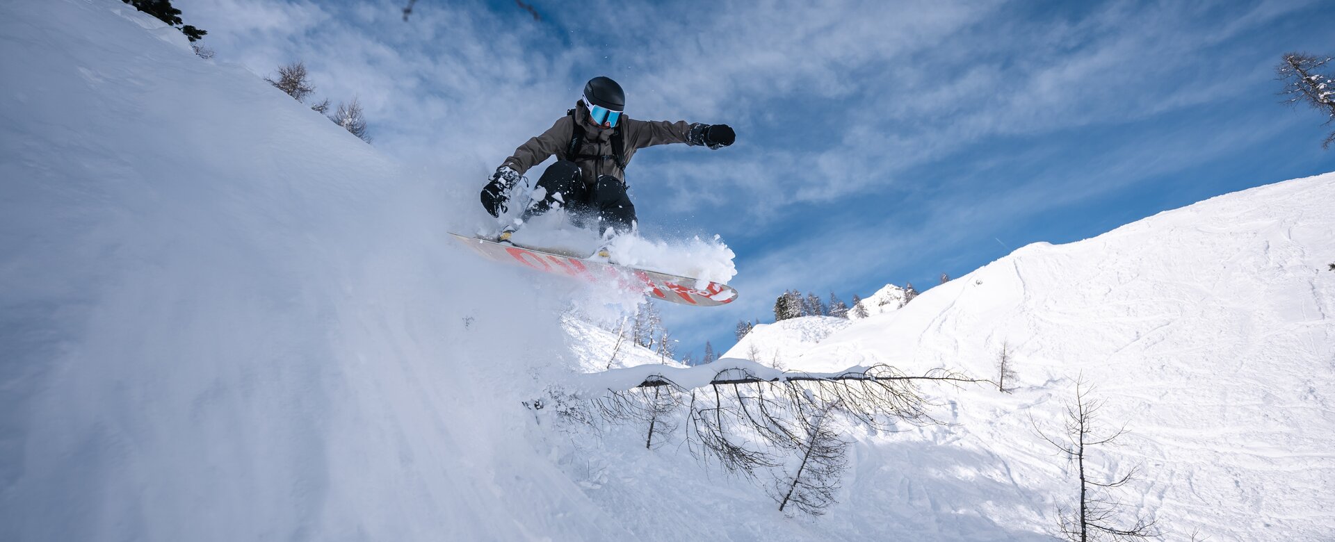 Snowboarder jumps in deep powder off snowy slope with trees in the backcountry of Zauchensee resort | © Liftgesellschaft Zauchensee/C.Schartner