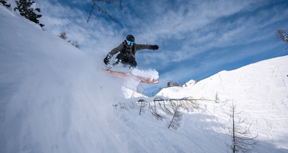 Snowboarder jumps in deep powder off snowy slope with trees in the backcountry of Zauchensee resort | © Liftgesellschaft Zauchensee/C.Schartner