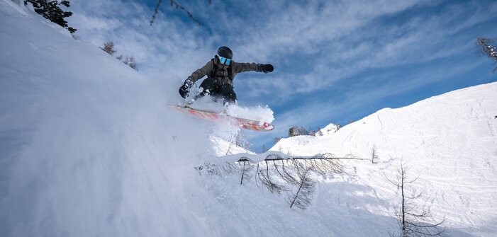 Snowboarder jumps in deep powder off snowy slope with trees in the backcountry of Zauchensee resort | © Liftgesellschaft Zauchensee/C.Schartner
