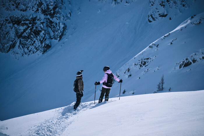 Two freeriders in helmets stand in deep snow, discussing their descent route on steep snowy slope | © Liftgesellschaft Zauchensee/C.Schartner