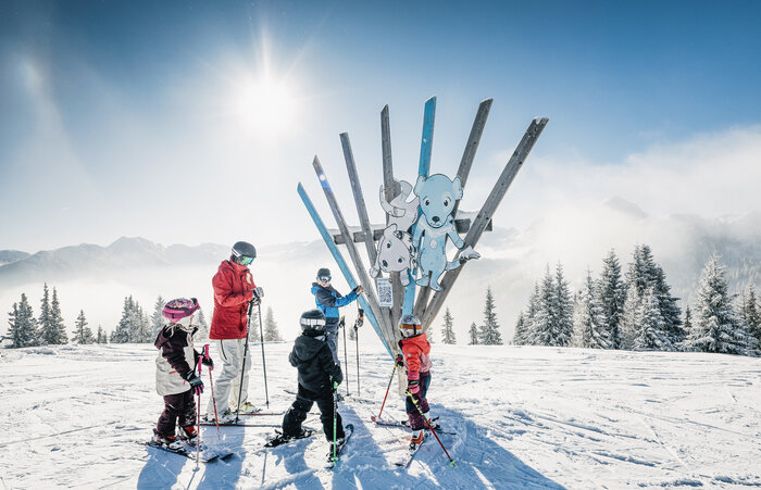 Kids with adult on skis in front of wooden sculpture with animals on Family Run at Shuttleberg resort | © Shuttleberg