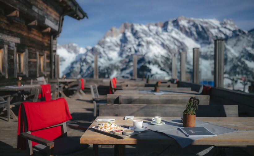 Kaiserschmarrn with powdered sugar and coffee on wooden table, empty terrace with Alpine backdrop | © Ski amadé