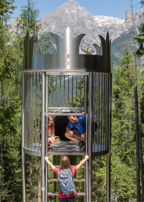 Girl climbs ladder to crown-shaped slide where dad and daughter wait, in the forest slide park at Natrun. | © Roland Haschka