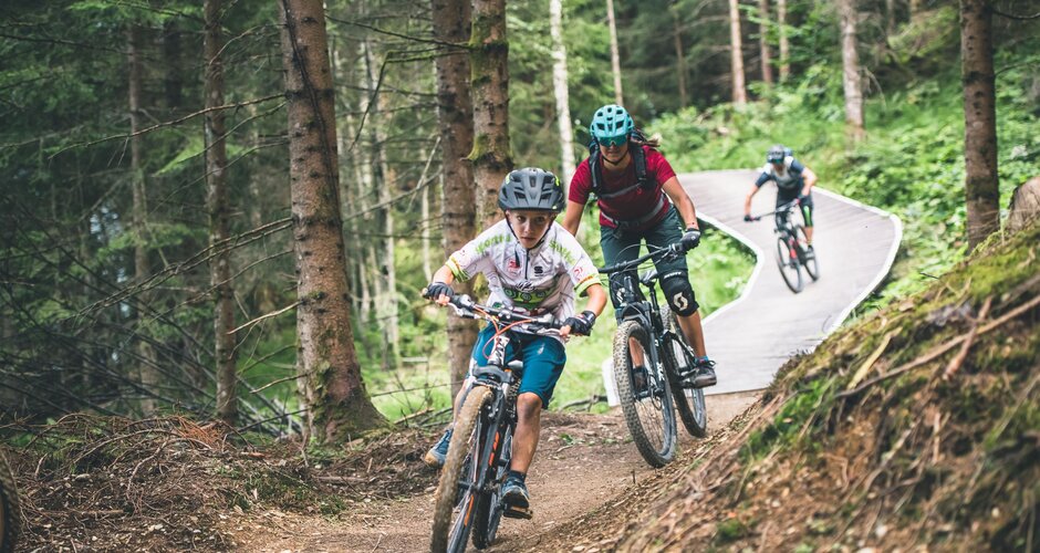 Mountainbiker fahren auf schmalem Flow Trail durch Wald mit Holzbrücken und Kurven