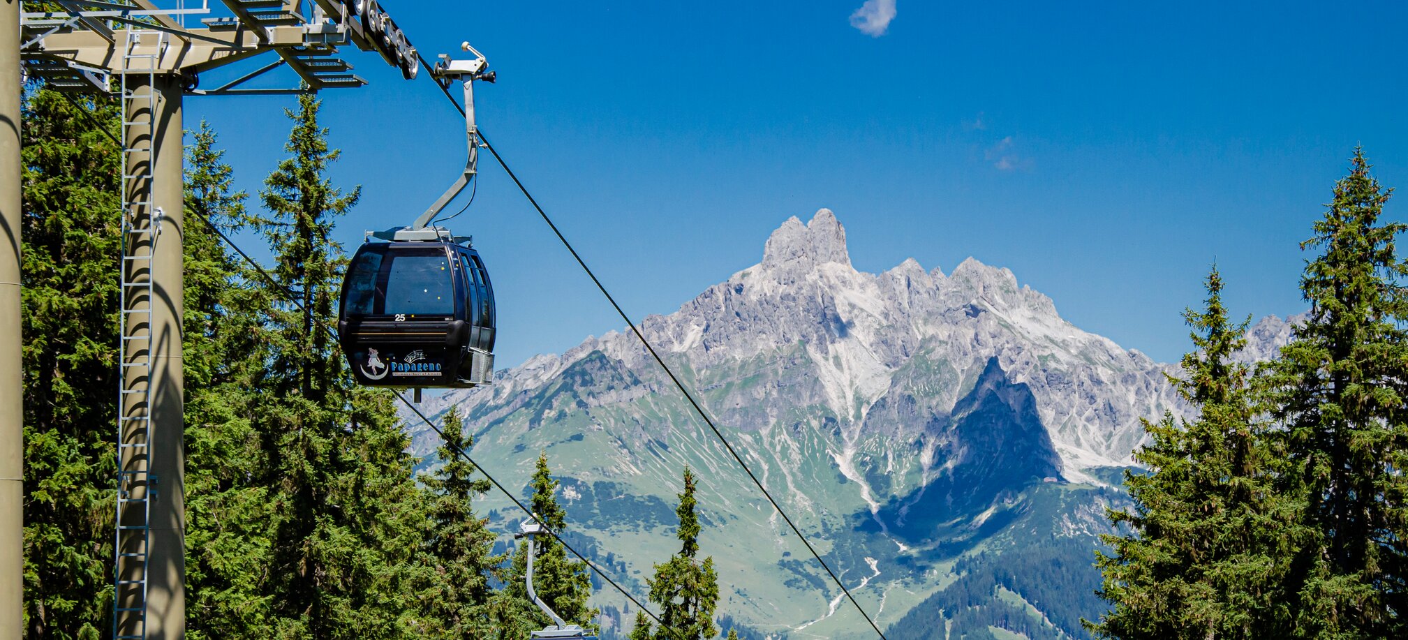 Papageno cable cars glide above conifer forest in Filzmoos, with a striking rocky mountain massif behind them. | © filzmoos.ski