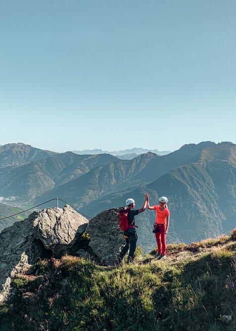 Two climbers give a high five on a secured via ferrata with wide view over the Gastein Valley | © Gasteiner Bergbahnen AG