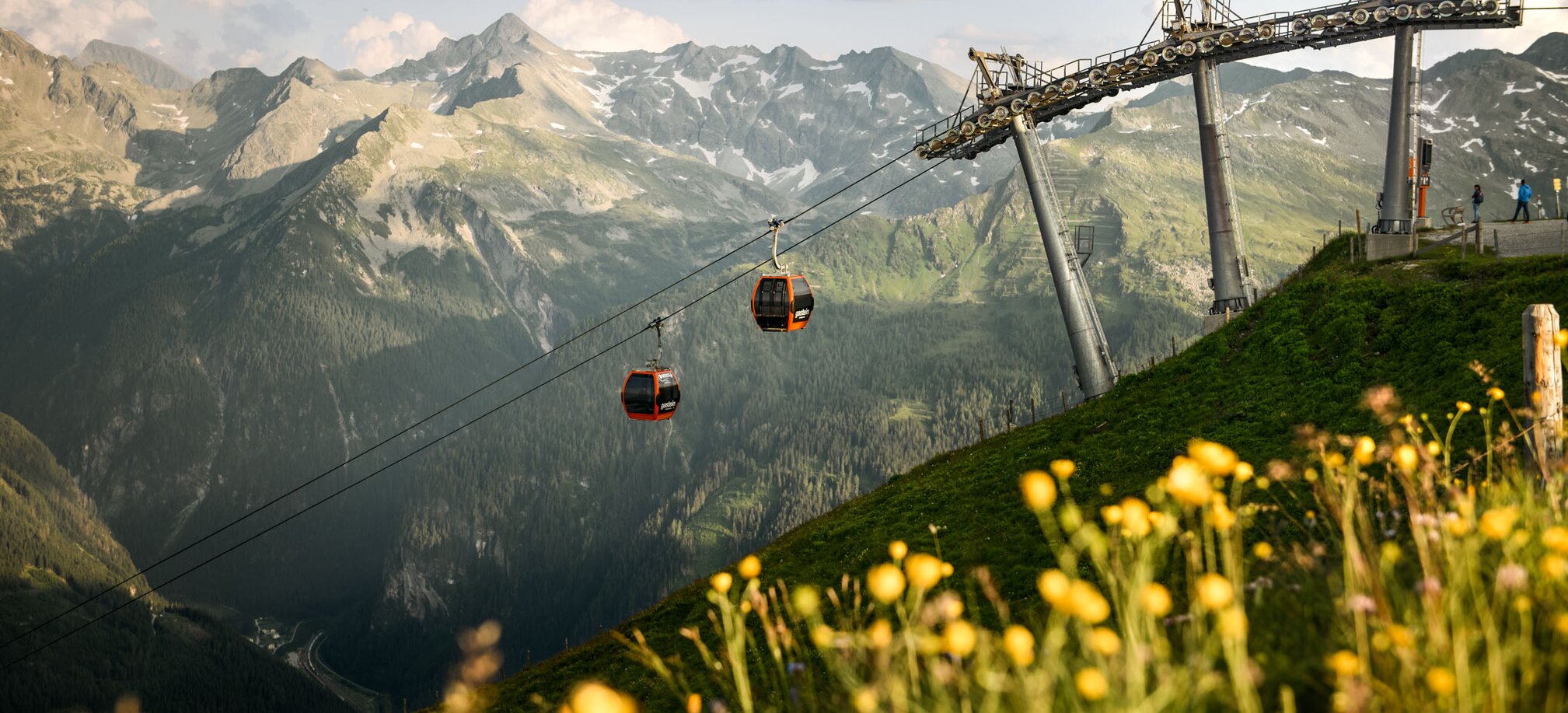 Two red gondolas of the gastein lift over blooming meadow and green valley in Gastein | © Gasteiner Bergbahnen AG, Marktl Photography