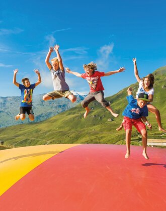 Kids jumping on colorful pillow at Schlossalm playground with mountain view and summer vibes | © Gasteiner Bergbahnen AG, Wolkersdorfer