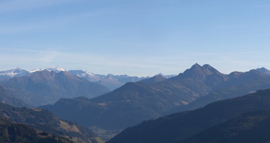 Panoramic view from Maria Alm of forested hills and snow-covered peaks in Salzburg region under autumn skies