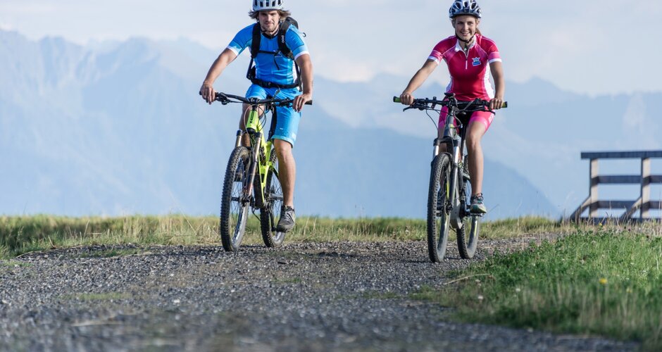 Two smiling e-bikers ride gravel trail with helmets and sportswear in the Hochkönig mountain region | © Christian Schartner