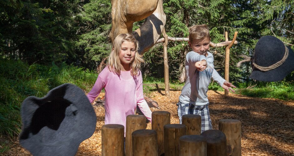 Two kids play hat toss with wooden stumps at alpine playground in the forest near Karbachalm in the Hochkönig region
