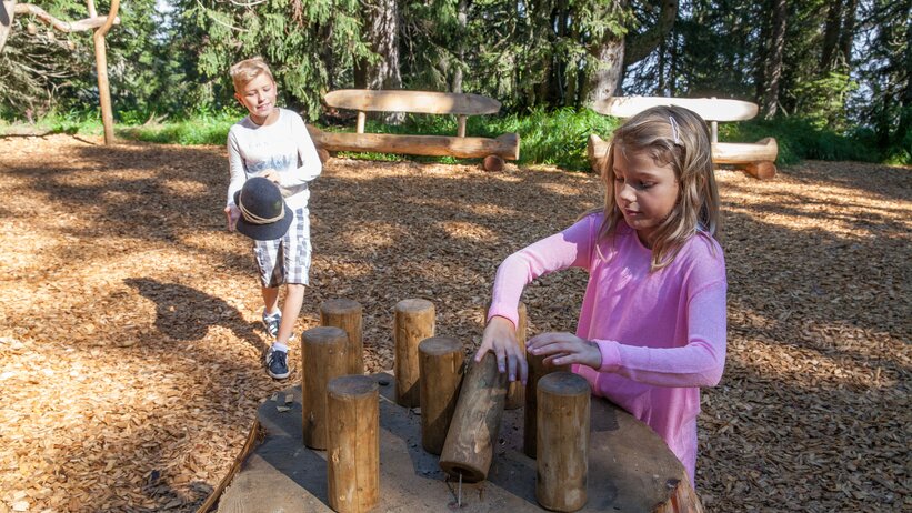 Two children play with wooden blocks at activity station in Hochkönig’s alpine playground, surrounded by forest