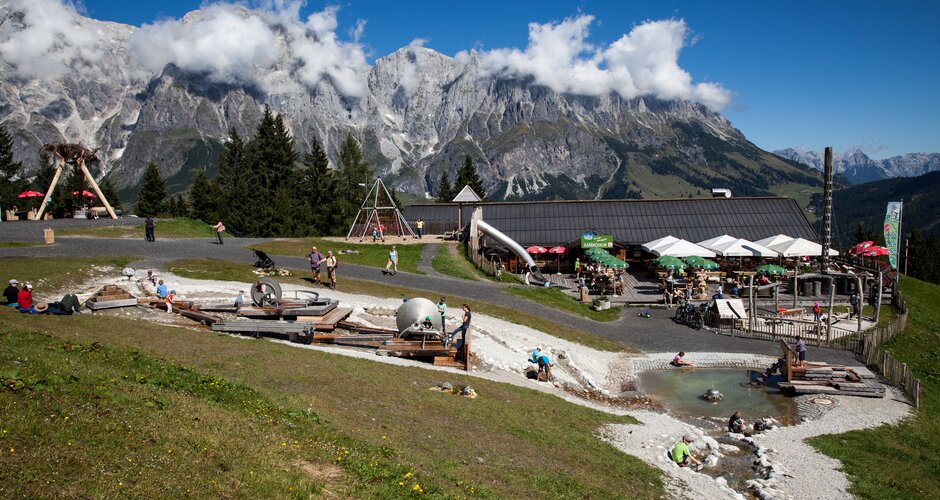 Children play at water park near Karbachalm hut with sunny terrace and Hochkönig mountains in the background