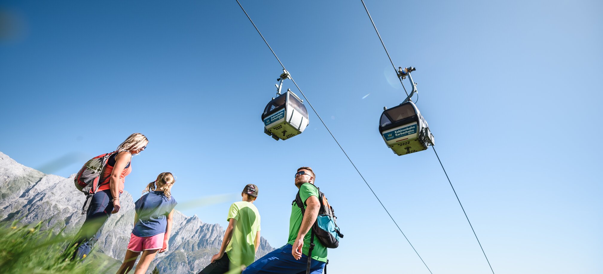 Hiking group below Karbachalm gondola with views of green valleys and the Hochkönig mountain range