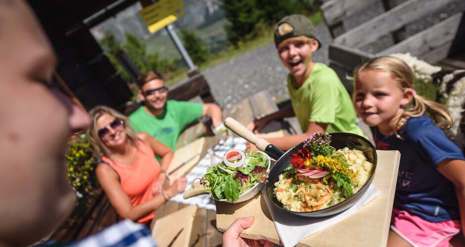 A server brings a dish with salad to a family on the sunny terrace at Karbachalm in Mühlbach. | © Hochkönig Bergbahnen
