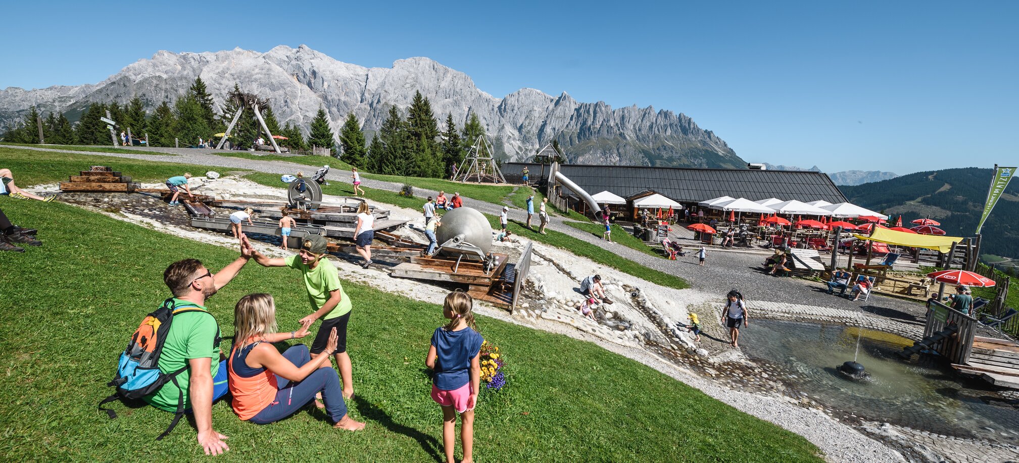 Families enjoying the water playground at Karbachalm with stunning Hochkönig backdrop on a sunny mountain day