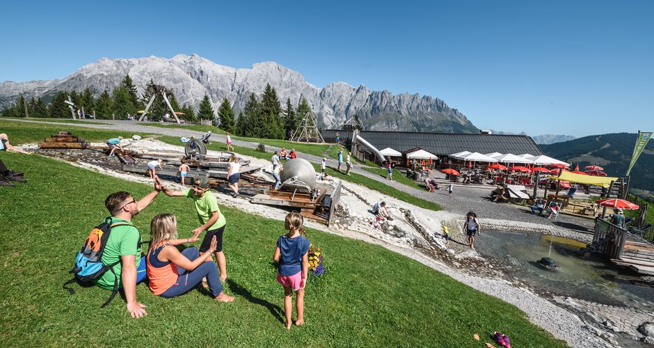 Families enjoying the water playground at Karbachalm with stunning Hochkönig backdrop on a sunny mountain day