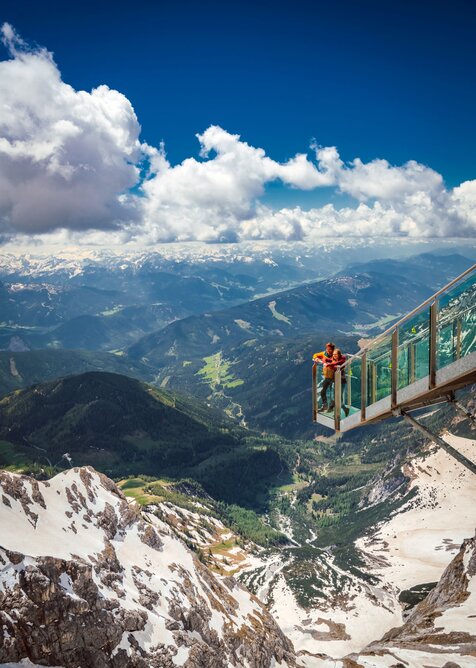 Two people stand on the glass Stairway to Nothingness at Dachstein, high above a deep green alpine valley. | © Christoph Huber