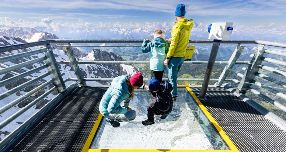 Family on Dachstein Sky Walk with glass floor, looking out over snowy mountains and green alpine valleys. | © Harald Steiner