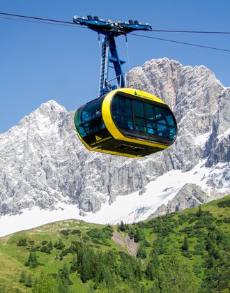 Yellow panorama gondola at Dachstein in front of glacier-covered cliffs and rugged alpine rocks