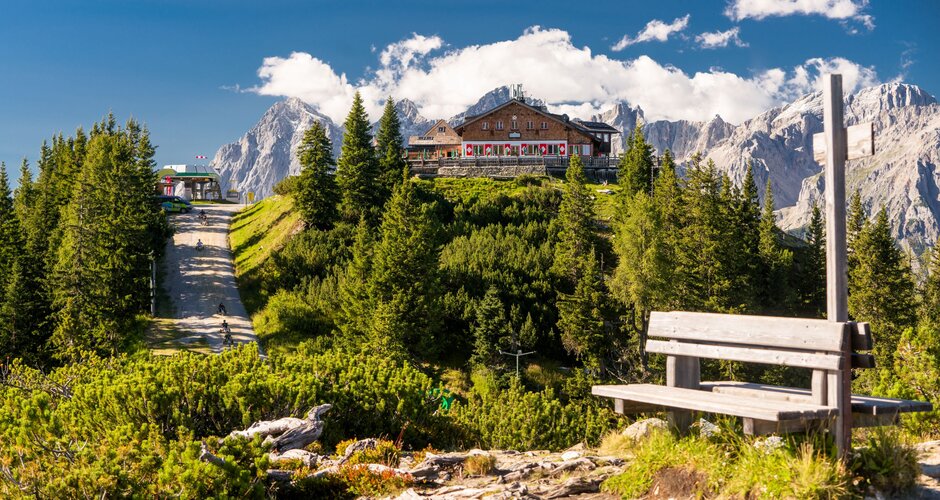 Alpine hut on Hochwurzen with terrace, surrounded by forest, peaks and fresh summer air under a blue sky. | © Christine Höflehner
