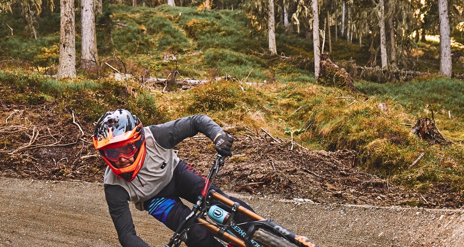 Ein Mountainbiker mit Helm und Brille fährt in Schräglage durch eine enge Kurve auf einem Waldtrail im Bikepark bei Sonnenlicht. | © Armin Walcher