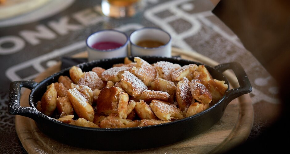 Fresh Kaiserschmarrn with powdered sugar in pan, served with sauces and beer on a rustic table at a Planai mountain hut. | © Dietmar Körbler