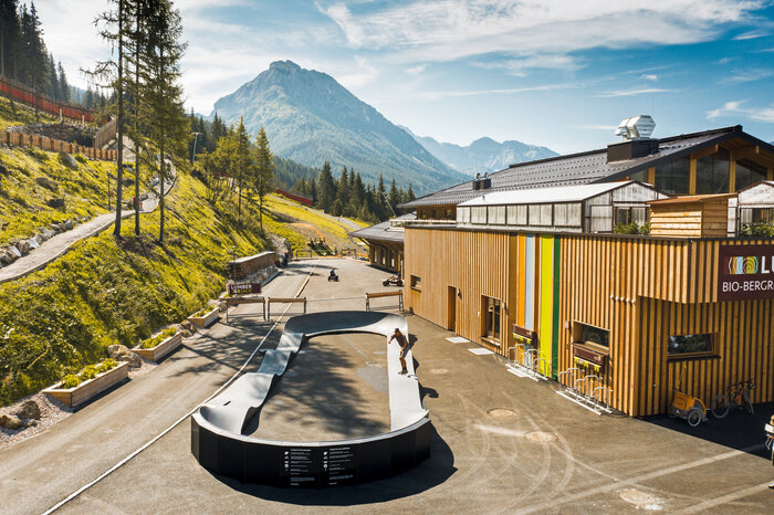 Skater on a pumptrack in front of the wooden bio-mountain restaurant in alpine surroundings. | © Shuttleberg