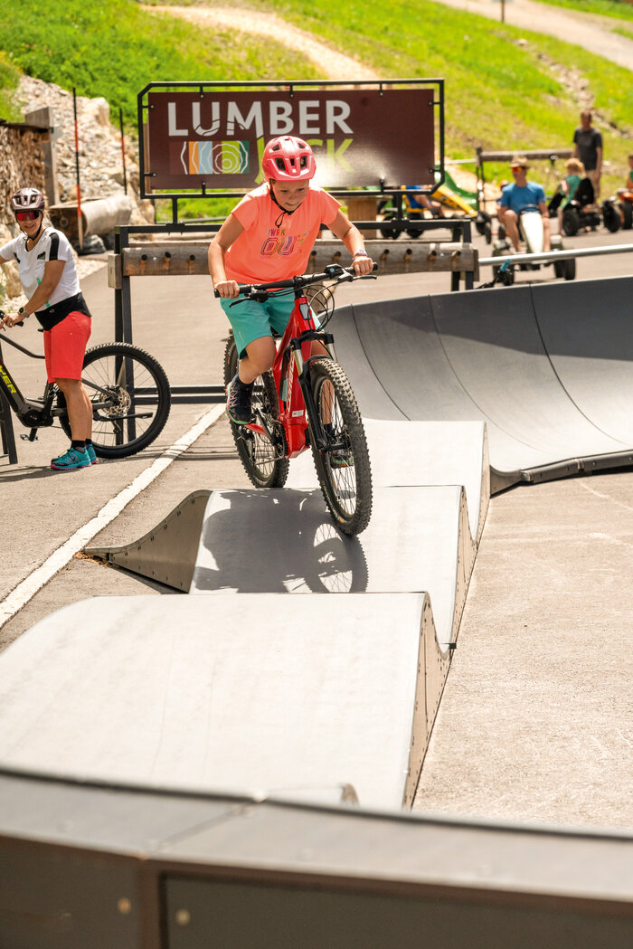 Kind fährt auf rotem Mountainbike mit Helm und pinkem Shirt über Pumptrack-Wellen | © Shuttleberg