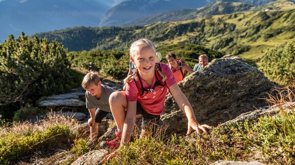 Smiling girl climbs rocky trail with her family on a summer hike in the alpine mountains near Flachau, Salzburger Land. | © TVB Flachau, Ulrich Grill