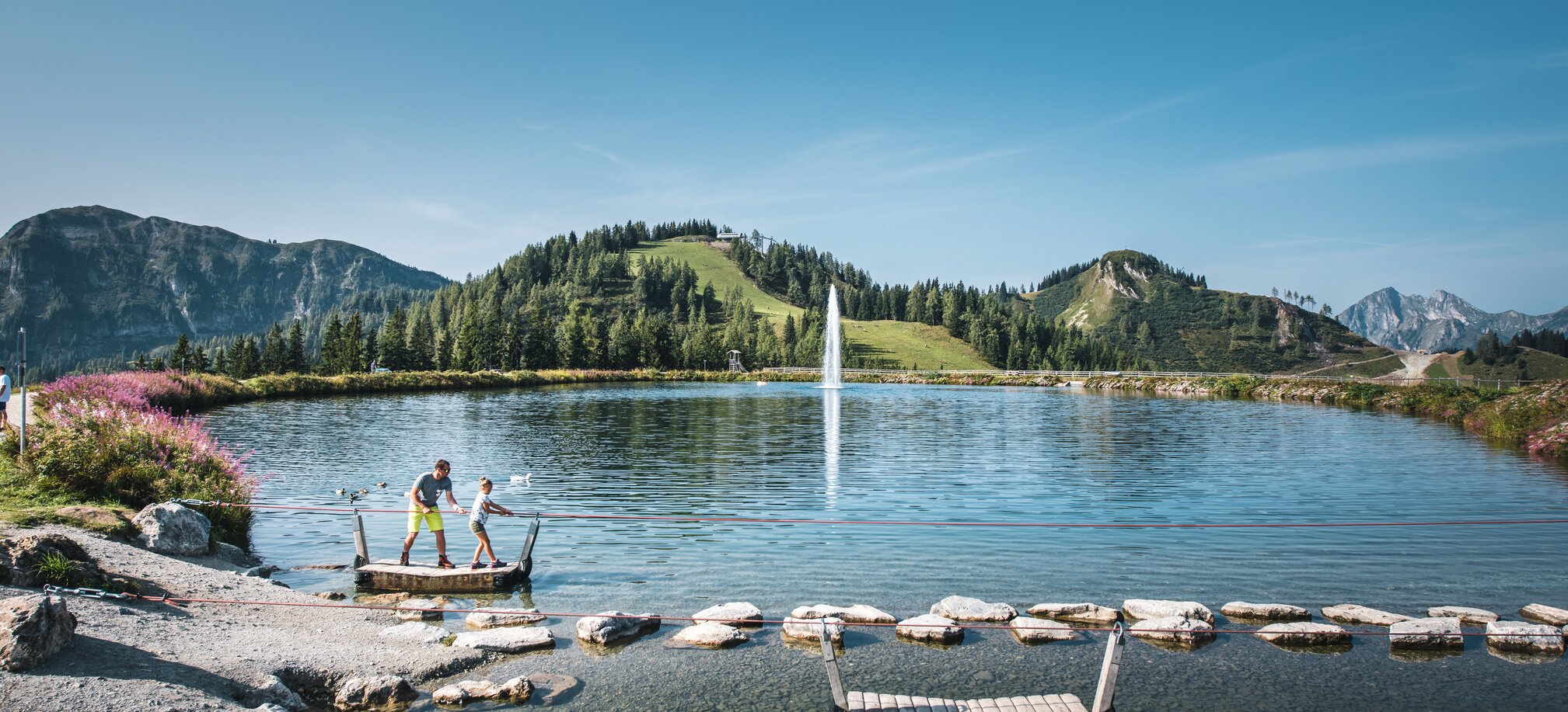 A father and his daughter stand on a raft and pull themselves to the opposite shore by a rope | © Christian Schartner