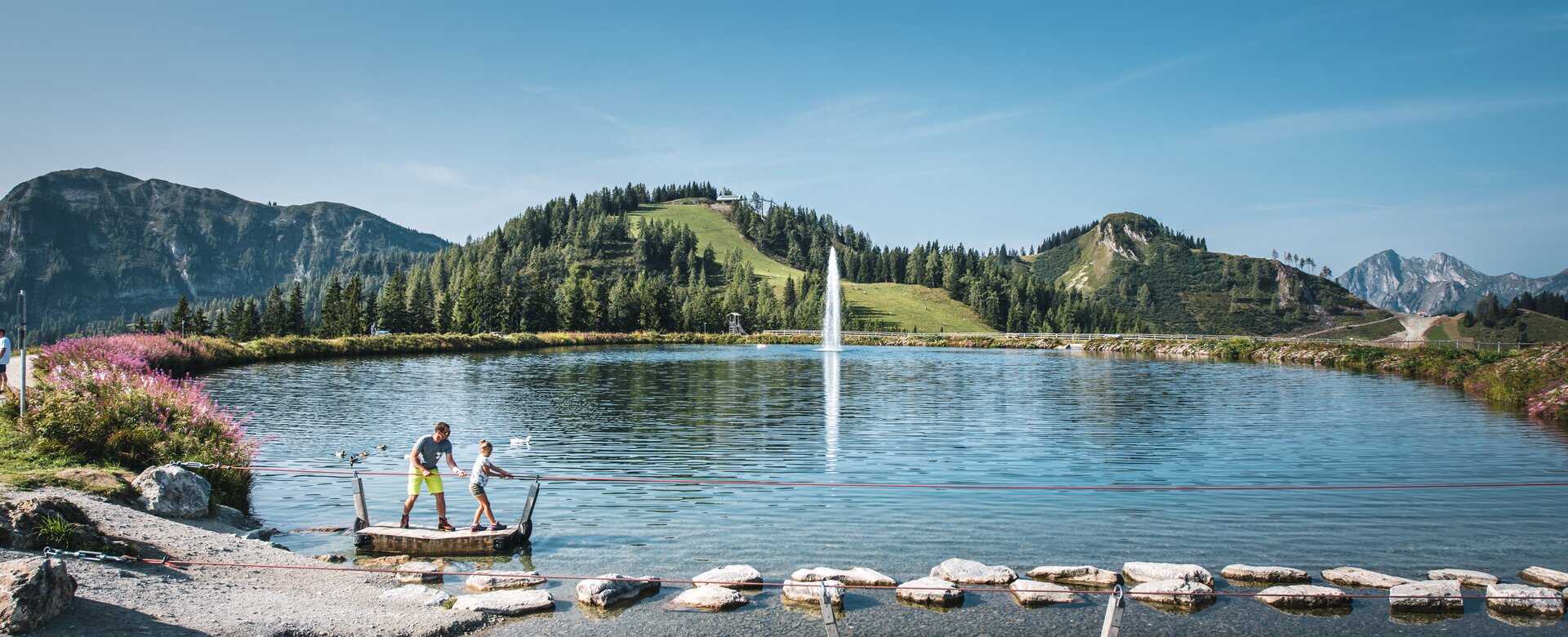 A father and his daughter stand on a raft and pull themselves to the opposite shore by a rope | © Christian Schartner
