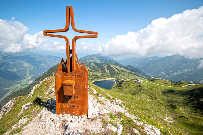 Rusty summit cross on Schwarzkopf with panoramic view of alpine scenery, reservoir lake and hiking trails in Zauchensee. | © Zauchensee Liftgesellschaft