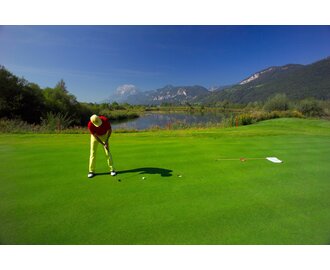 Golfer putting on vibrant green, with lake, summer scenery and the towering Grimming mountain in the background. | © Hagspiel Erich