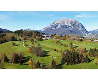 Expansive golf course in Pichlarn with hotel at center, set against dramatic Grimming mountain backdrop in summer. | © Golf & Country Club Schloss Pichlarn