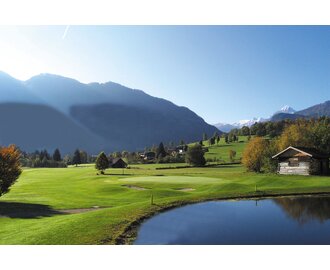 Scenic view of Golfclub Goldegg with pond, alpine hut, green fairways and snow-covered mountains in the background. | © Golfclub Goldegg