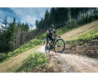 Biker with helmet and gear on Flowtrail One in Maria Alm, gondola and forest in the background | © Schartner