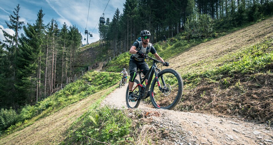 Biker with helmet and gear on Flowtrail One in Maria Alm, gondola and forest in the background | © Schartner