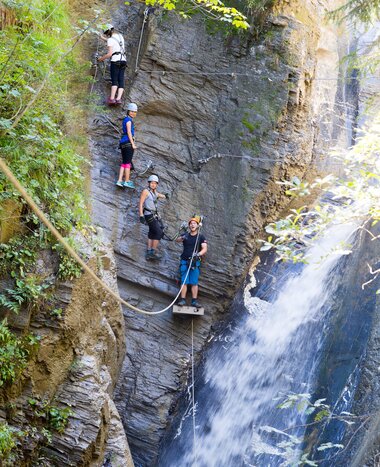 Several climbers ascend a steep rock face alongside a waterfall on a secured via ferrata route in Wagrain-Kleinarl | © Wagrain-Kleinarl